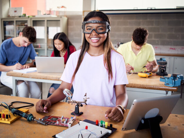 Looking at camera portrait of a young student wearing safety goggles in technical vocational training college, the lesson in High School. Education and technology concept. Looking at camera portrait of a young student wearing safety goggles in technical vocational training college, the lesson in High School. Education and technology concept. High quality photo